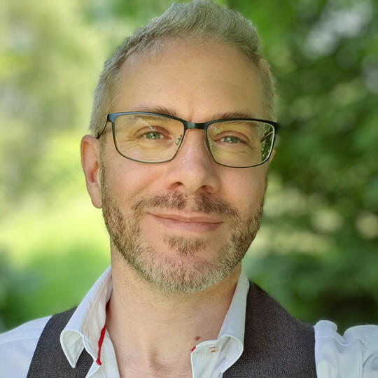 Finbarre Snarey Portrait of Finbarre Snarey wearing glasses and a white shirt with a waistcoat, photographed outdoors.